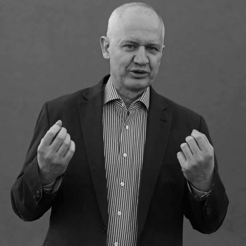 Senior businessman in suit jacket making a gesture, in black and white.